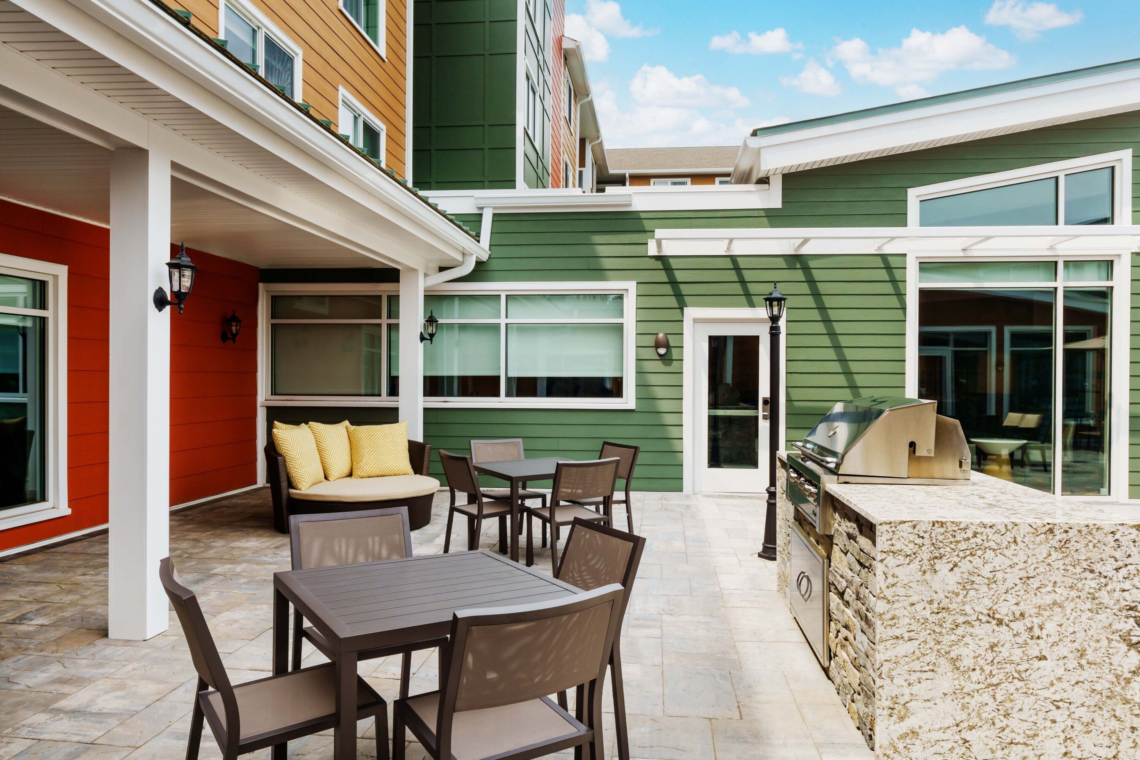 A patio area with a table and chairs, a grill, and a cushioned seating area.