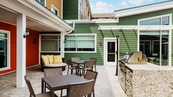 A patio area with a table and chairs, a grill, and a cushioned seating area.