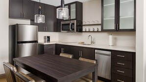 A modern kitchen with dark cabinetry, stainless steel appliances, a dining table with chairs, and pendant lighting. - Residence Inn by Marriott New Haven Hamden (Hamden)