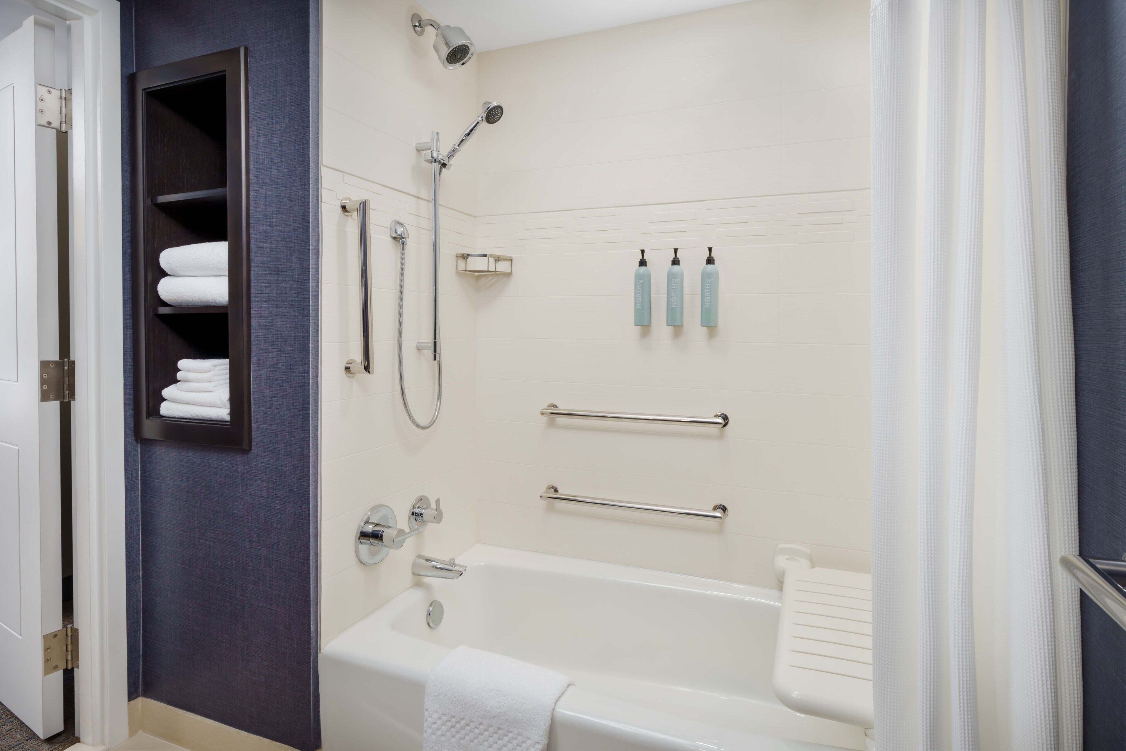 A bathroom with a bathtub, a shower, and a towel rack with folded towels.