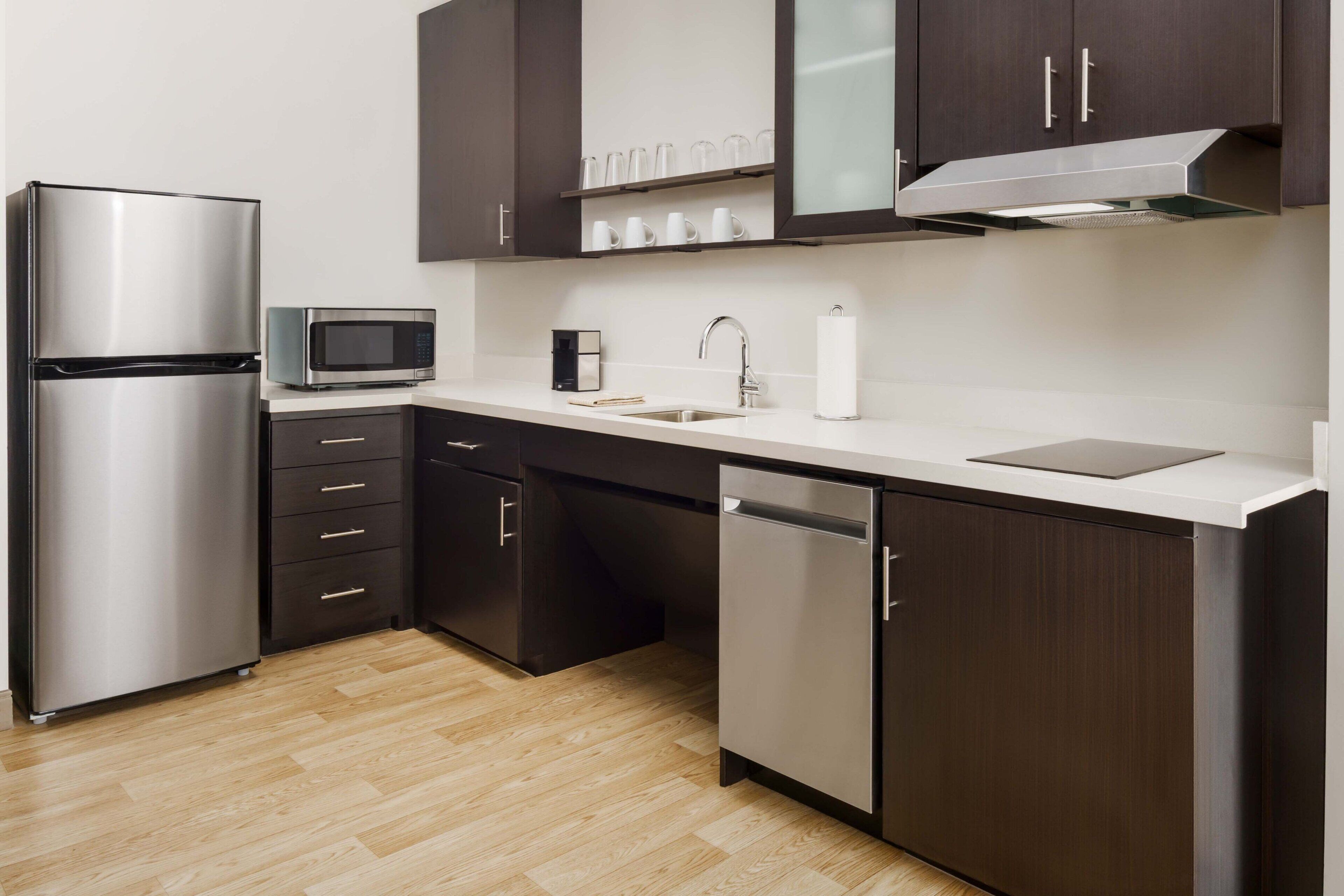 A modern kitchen with stainless steel appliances, dark cabinetry, and a wooden floor.