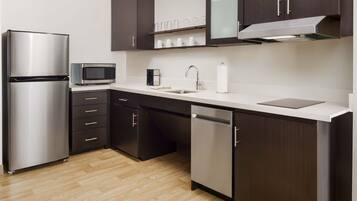 A modern kitchen with stainless steel appliances, dark cabinetry, and a wooden floor.