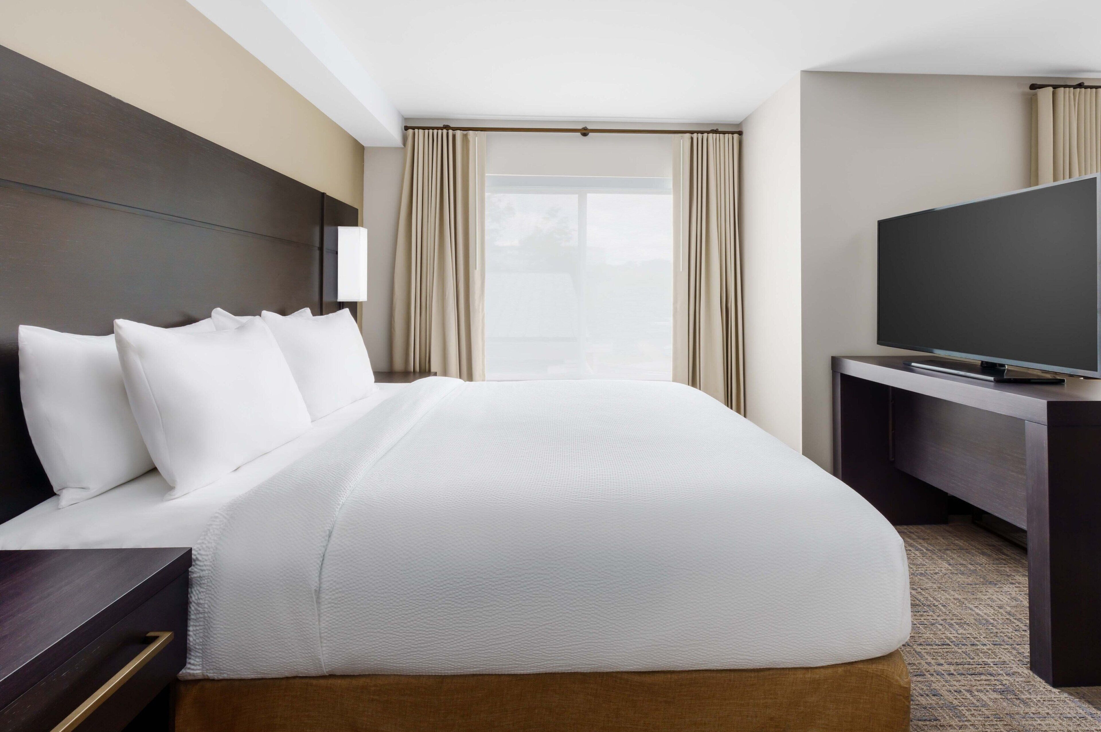 Habitación de hotel con una cama grande, televisión de pantalla plana, escritorio y ventana con cortinas.