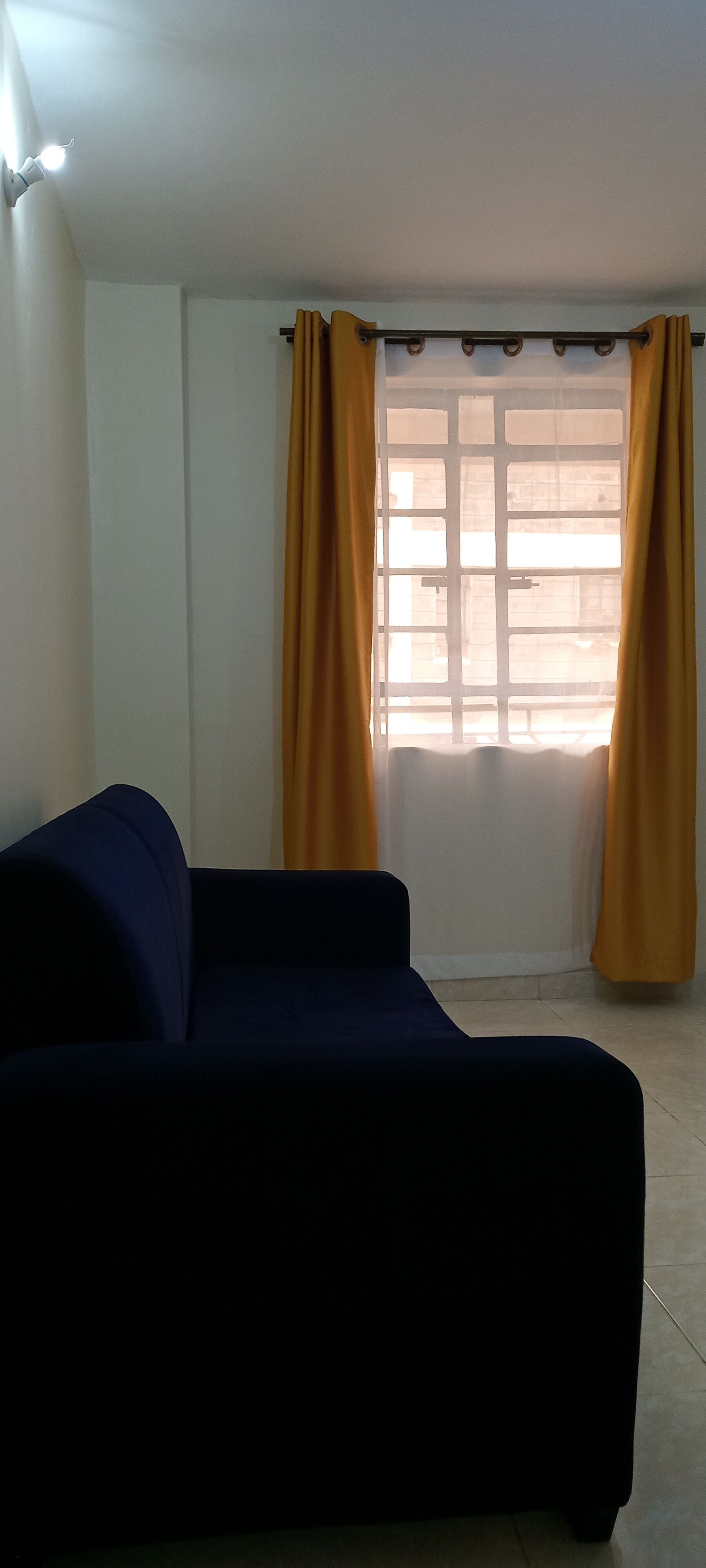 Una habitación con un sofá oscuro, una ventana con cortinas amarillas y una pared blanca.