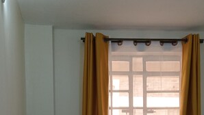 Ein Zimmer mit einem dunkelgrauen Sofa, einem Fenster mit gelben Vorhängen und einer weißen Wand.