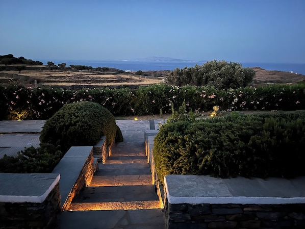 Una escalera de piedra que lleva a una terraza con vistas al mar y colinas distantes.