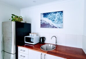 Kitchen features a stainless steel refrigerator, microwave, and coffee maker on the countertop, along with a sink under a wooden countertop.