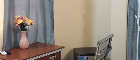 Quarto com escrivaninha, cadeira, televisão e uma pequena mesa com um vaso de flores.