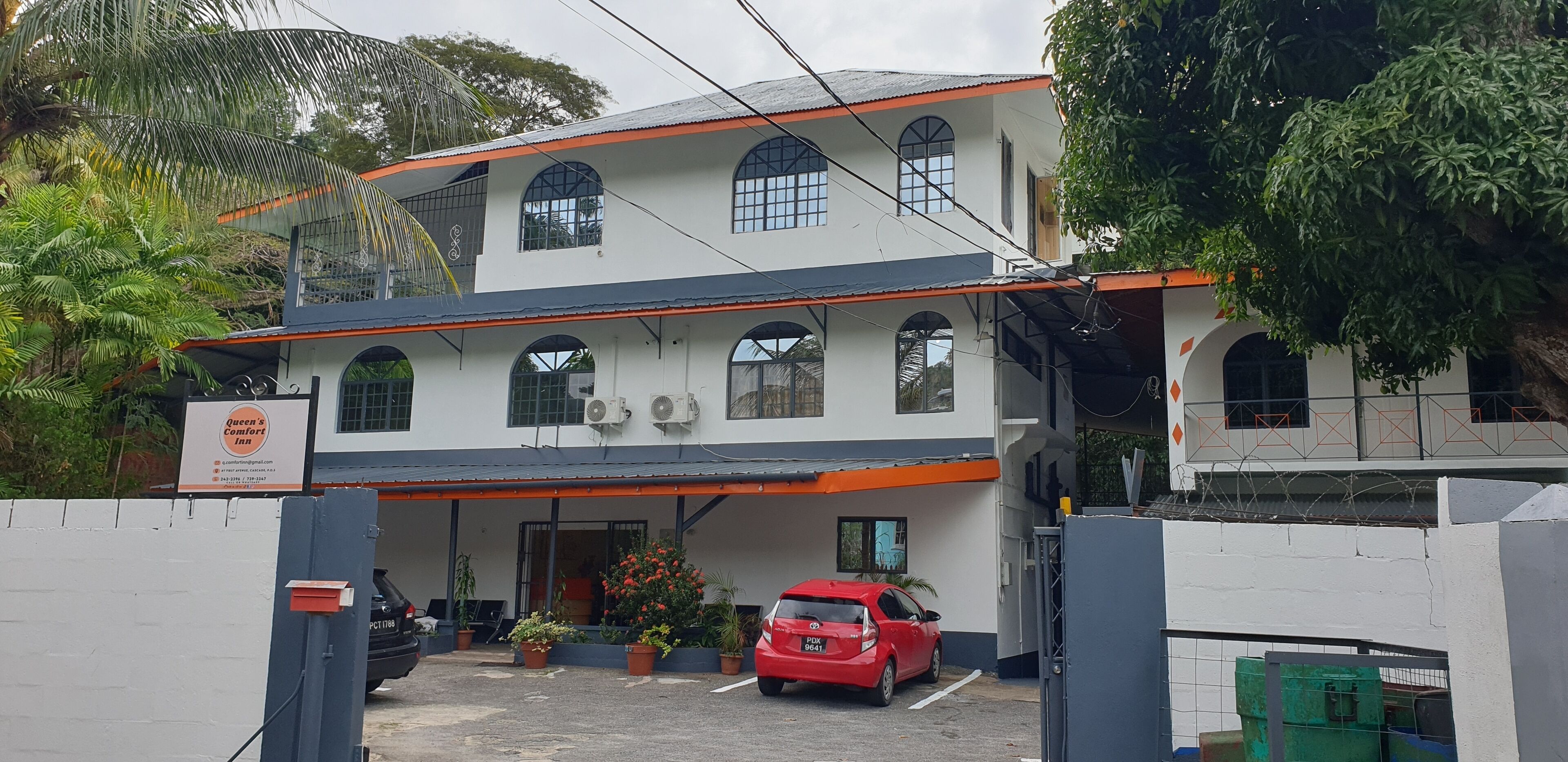 Um edifício de dois andares com uma placa indicando 'Queen's Comfort Inn' e um carro vermelho estacionado em frente.