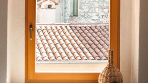 Vista a través de una ventana que muestra una puerta de madera, un tejado de baldosas y una pared de piedra.