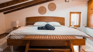 Un dormitorio con una cama de madera, cabecera, dos adornos tejidos en la pared, una mesita de noche con lámpara y un armario.