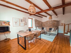 A cozy living room with a stone wall, wooden beams, a dining area with wicker chairs, and a sofa with patterned cushions. - Casa dell'armonia - The oasis of peace in the center of Rovinj (Rovinj)