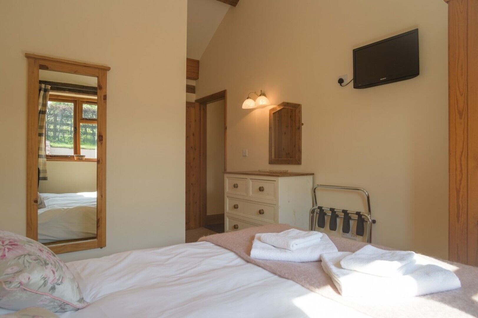 A bedroom with a bed, a dresser, a mirror, and a TV.