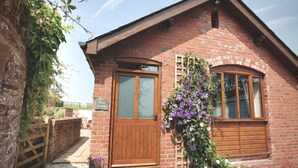A brick building with a wooden door and windows, a sign reading "Belli Stable," and a potted plant with purple flowers. - Beili Stable, a spacious country barn near Monmouth with spectacular views (The Hendre)