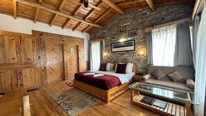 Quarto com piso de madeira, uma cama, um sofá, uma mesa de vidro e uma parede de pedra.