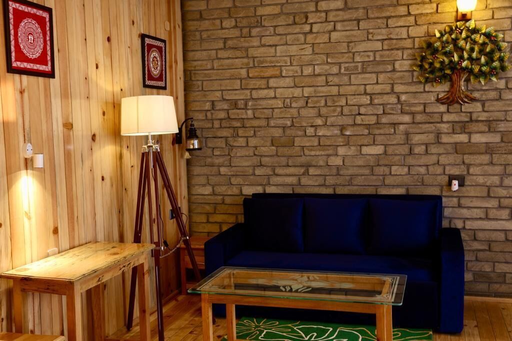 A cozy living room with a brick wall, a blue sofa, a glass coffee table, and a wooden side table.