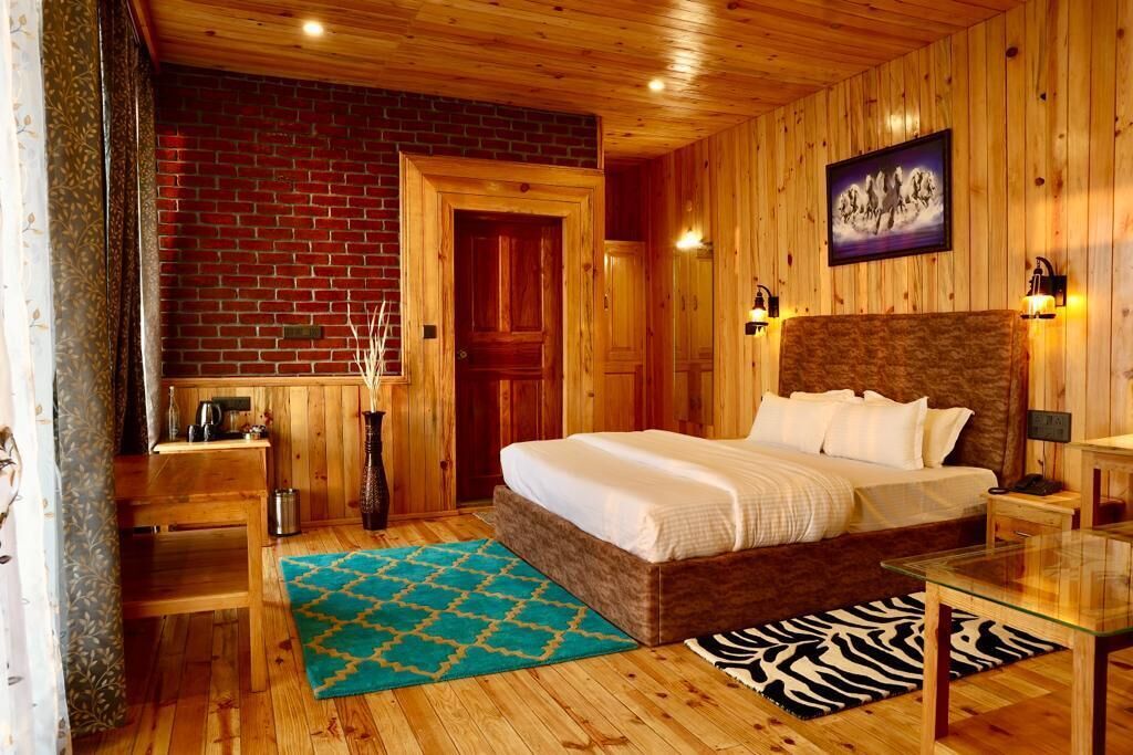 Un dormitorio con paneles de madera, una cama grande, una mesita de noche, una pequeña mesa, un tapete con estampado de cebra y una pared de ladrillo rojo.
