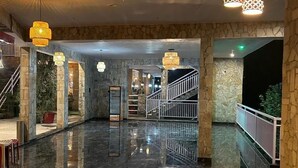 Um hall amplo com piso de mármore polido, paredes de pedra e escadaria para os andares superiores.