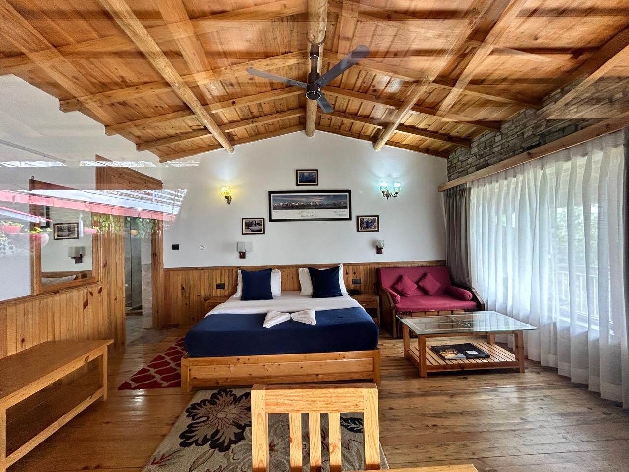 A wooden-floored room with a bed, a sofa, a coffee table, and a ceiling fan.