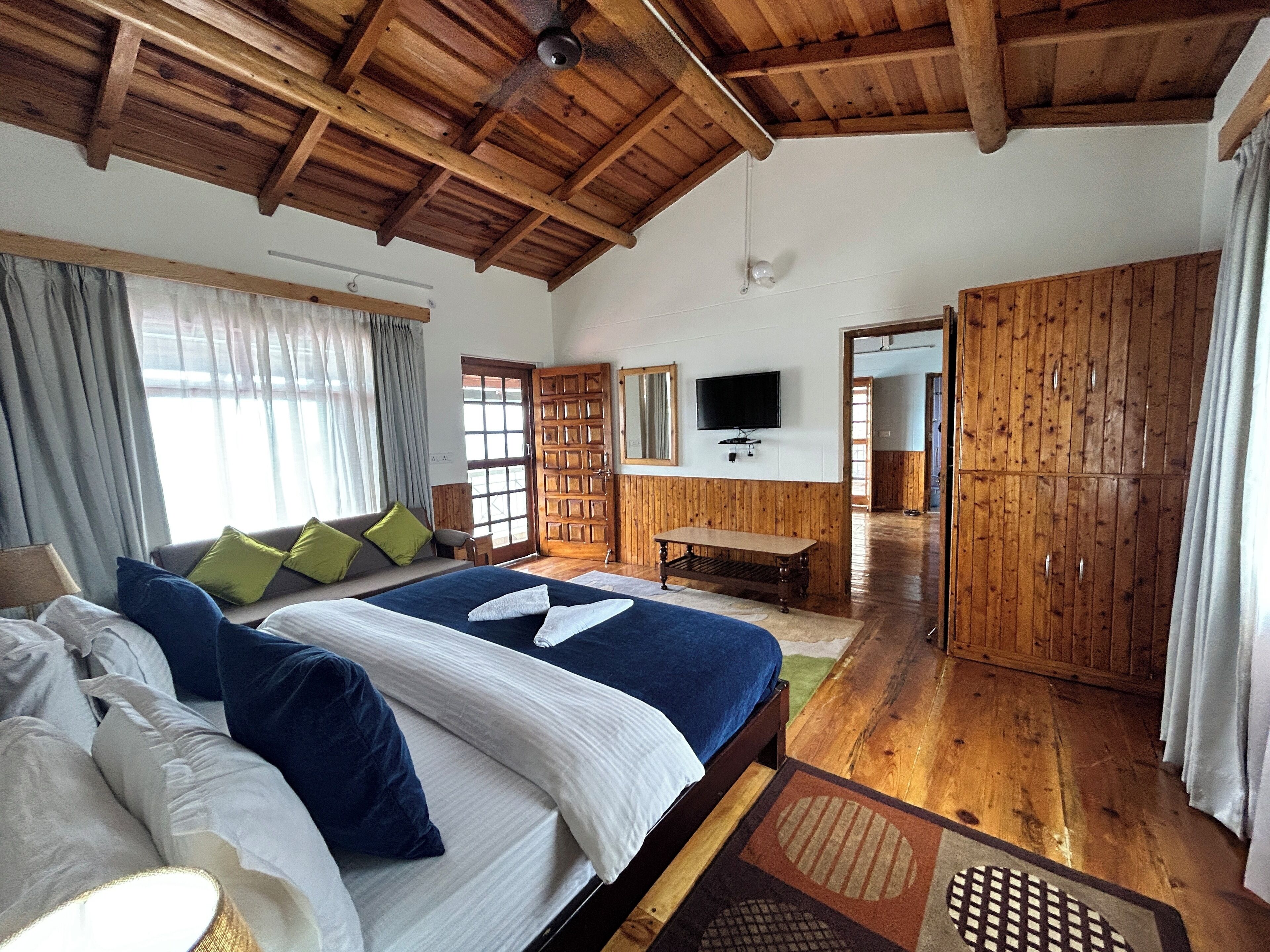 Une chambre spacieuse avec un grand lit, un plafond en bois et un téléviseur fixé au mur.