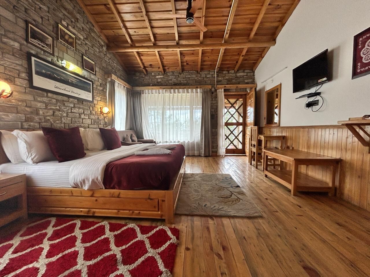 A cozy bedroom with a wooden bed, a stone wall, and a TV mounted on the wall.