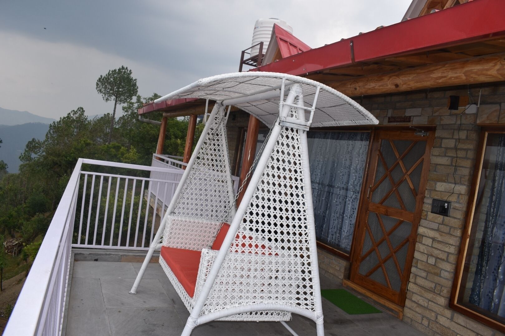 Una silla colgante de mimbre blanca con un cojín rojo en un balcón.