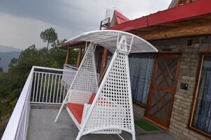 Una silla colgante de mimbre blanca con un cojín rojo en un balcón.