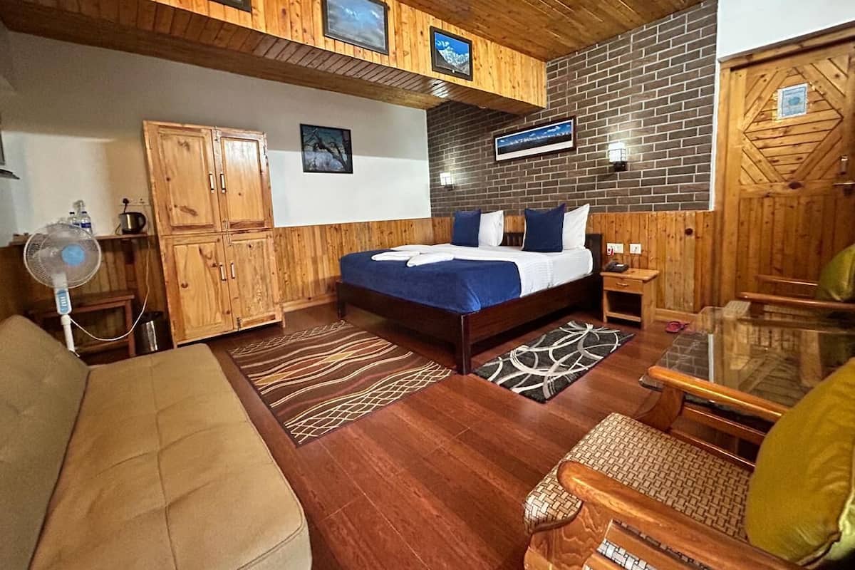 A wooden-floored bedroom with a bed, a wooden wardrobe, a glass table, and a sofa.