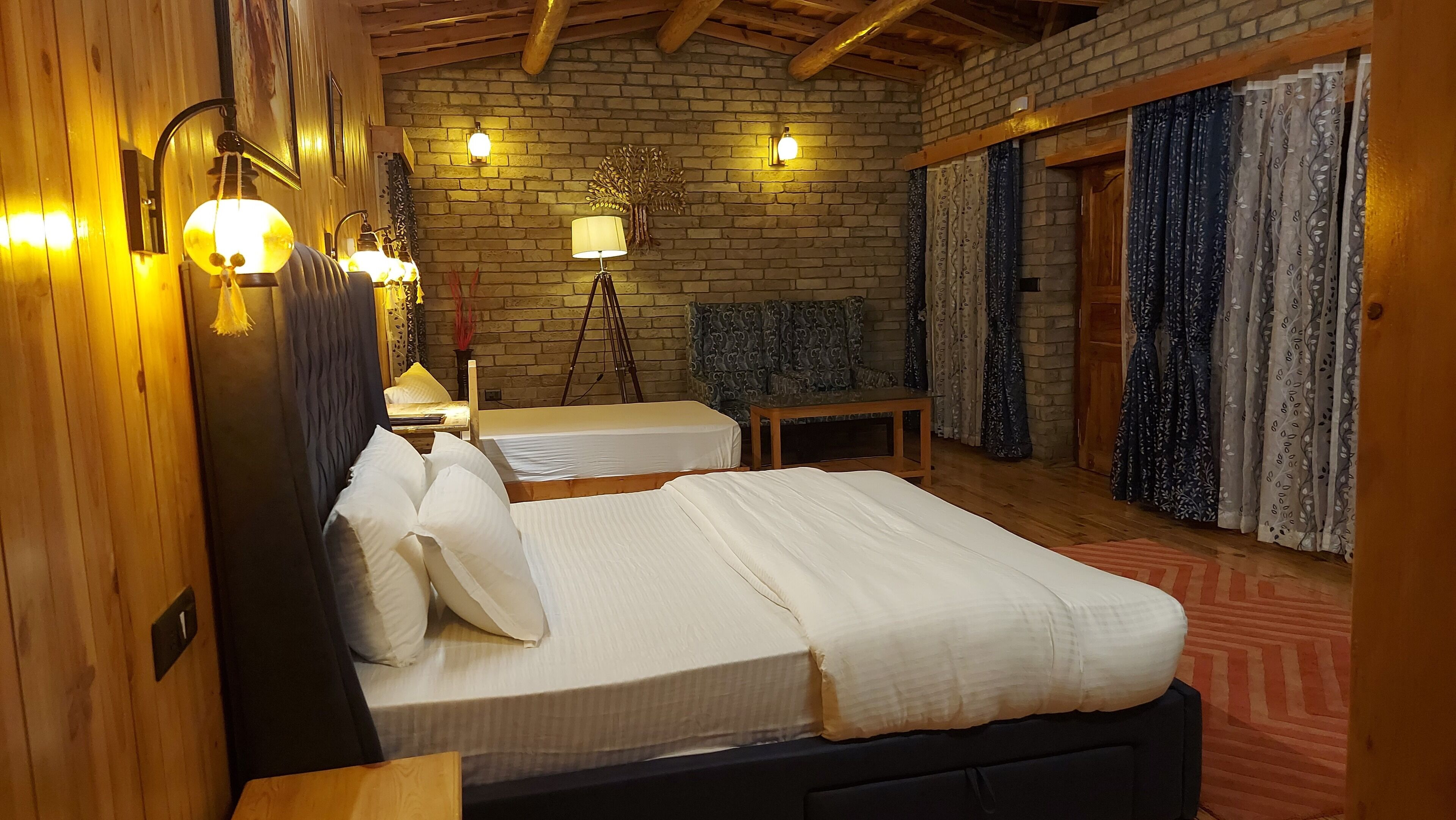 Quarto com duas camas, teto de madeira, paredes de tijolo e cortina estampada.