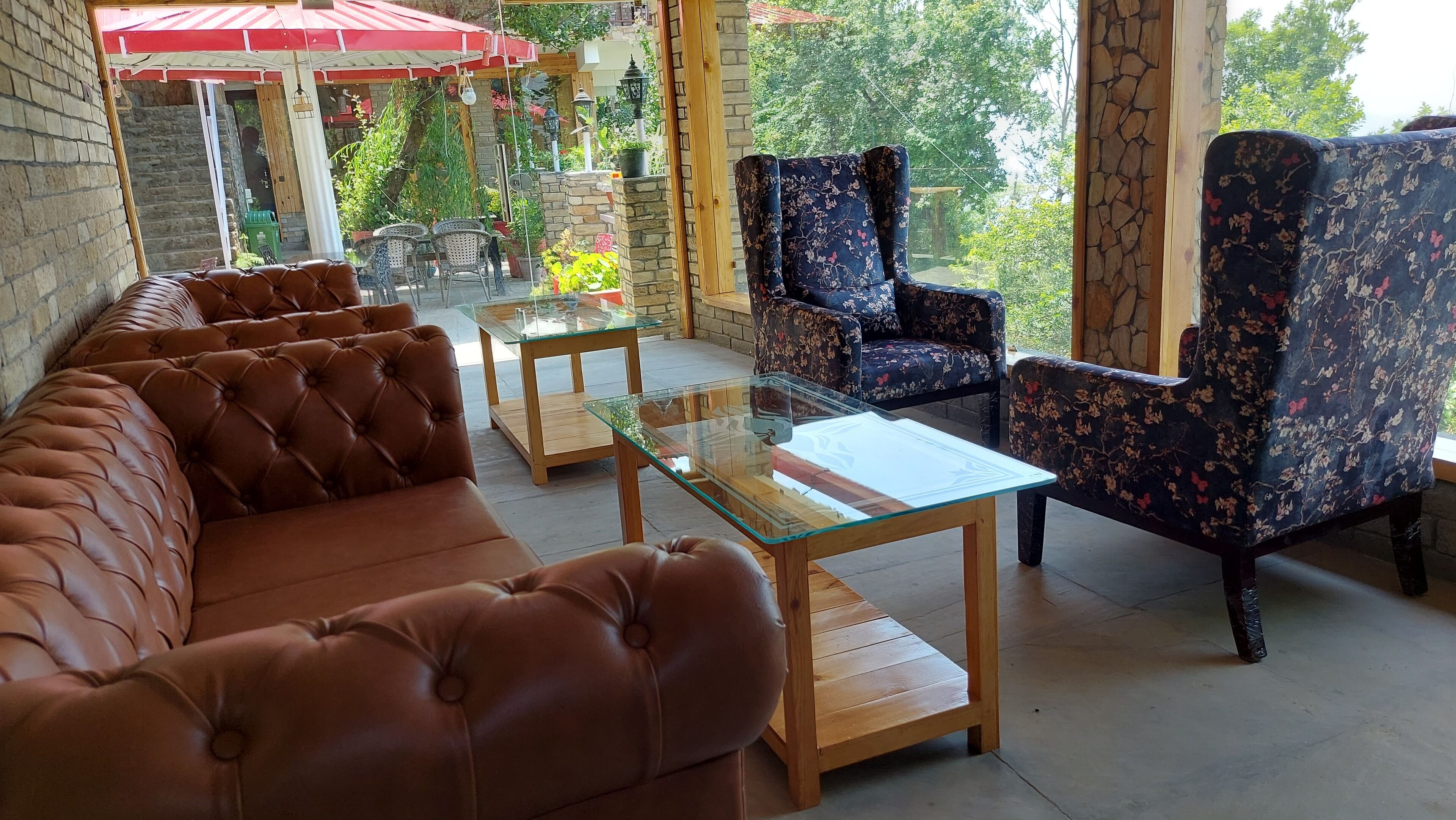 A cozy indoor seating area with a brown leather sofa, a glass-top coffee table, and floral-patterned armchairs.