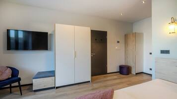 Ein modernes Hotelzimmer mit Flachbildfernseher, Kleiderschrank, Bett und einer kleinen Sitzecke.