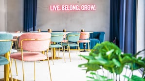 A modern dining area with teal and pink chairs, a blue sofa, and a neon sign reading "LIVE. BELONG. GROW." - The Base Berlin ONE (Berlin)