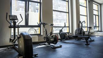 Ein Fitnessraum mit Ergometer und Crosstrainern, großen Fenstern und einem sauberen Boden.