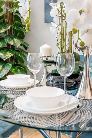 A dining table set with white plates, silverware, and clear glassware, surrounded by lush green plants and white orchids. - Lofts - Downtown Luxury - 5 Min Walk To Dubai Fountain! (Dubai)