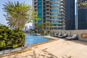 A rooftop pool area with lounge chairs, a swimming pool, and modern buildings in the background. - Lofts - Downtown Luxury - 5 Min Walk To Dubai Fountain! (Dubai)