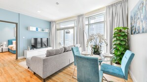 Un salon moderne avec un canapé gris, des fauteuils bleus, un téléviseur et une table à manger agrémentée d’une plante.
