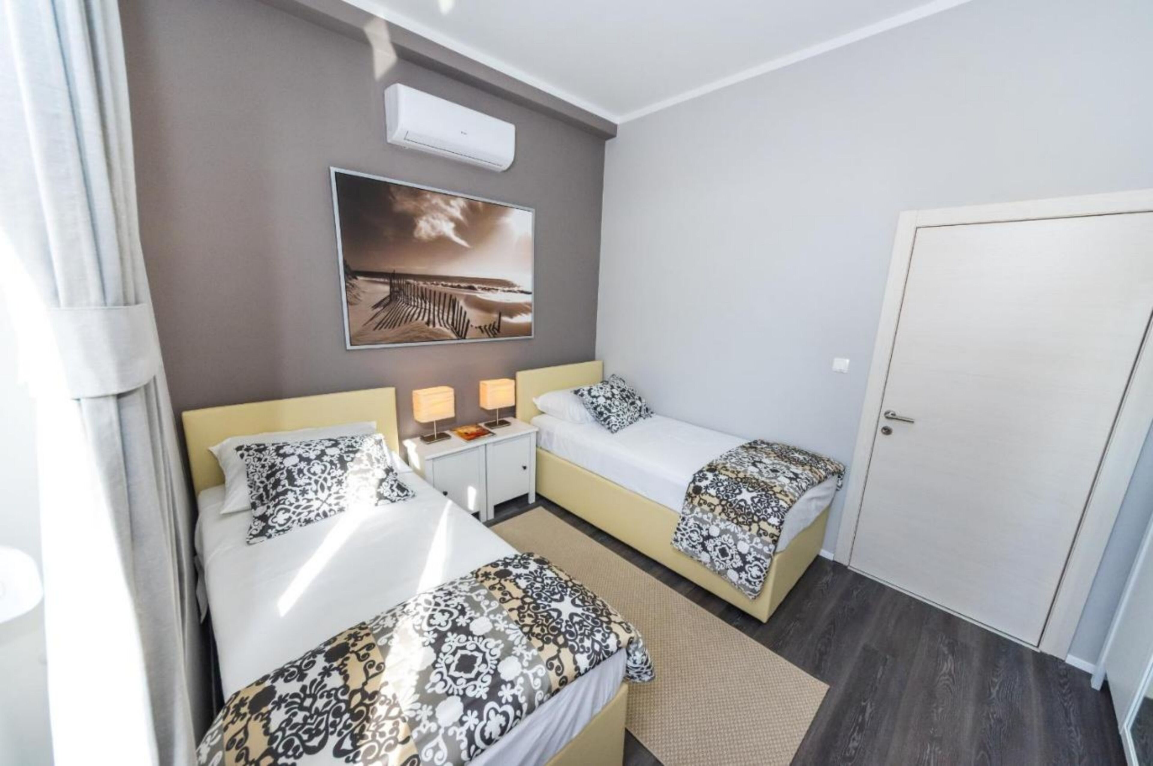 Ein Hotelzimmer mit zwei Betten, einem Nachttisch, einer Wandklimaanlage und einer Tür.