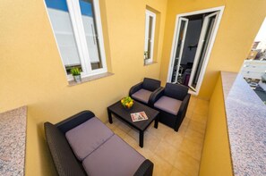 A small balcony with two cushioned chairs and a table, a small window, and a door leading to an interior space.