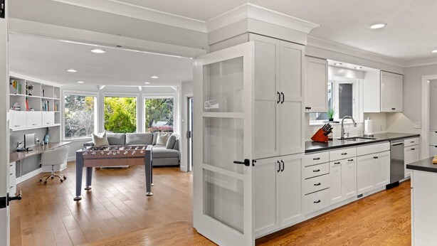 A modern kitchen with white cabinetry, a dining area with a table and chairs, and a view of greenery outside.