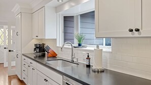 A modern kitchen with white cabinets, a black countertop, a sink, and a window with blinds.