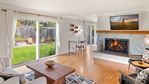 A spacious living room with a fireplace, a dining area, and a view of the backyard.
