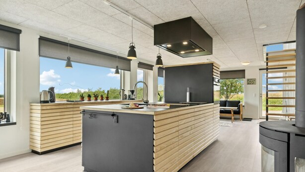 A modern kitchen with a central island, pendant lighting, and a large window offering a view of the outdoors.