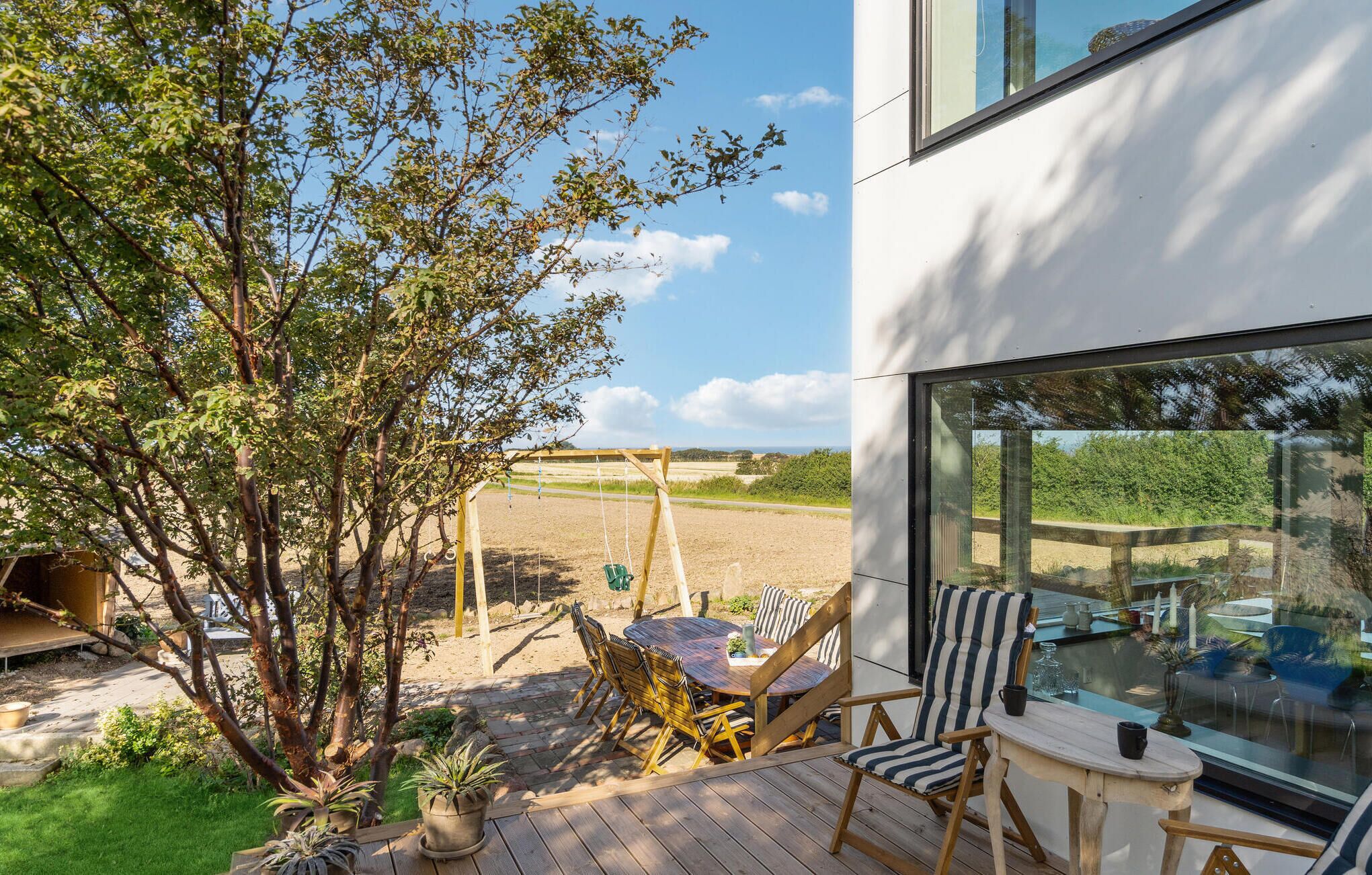 A modern outdoor patio with a swing set, a round table, and striped chairs.