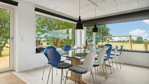A modern dining area with a glass table, blue and white chairs, and pendant lighting.