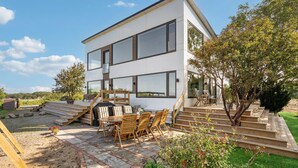 A modern two-story house with large windows, a patio with outdoor furniture, and a well-maintained garden.