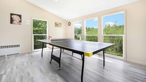 A room with a ping pong table, large windows, and a skylight. - Garden View Home (Tobyhanna)