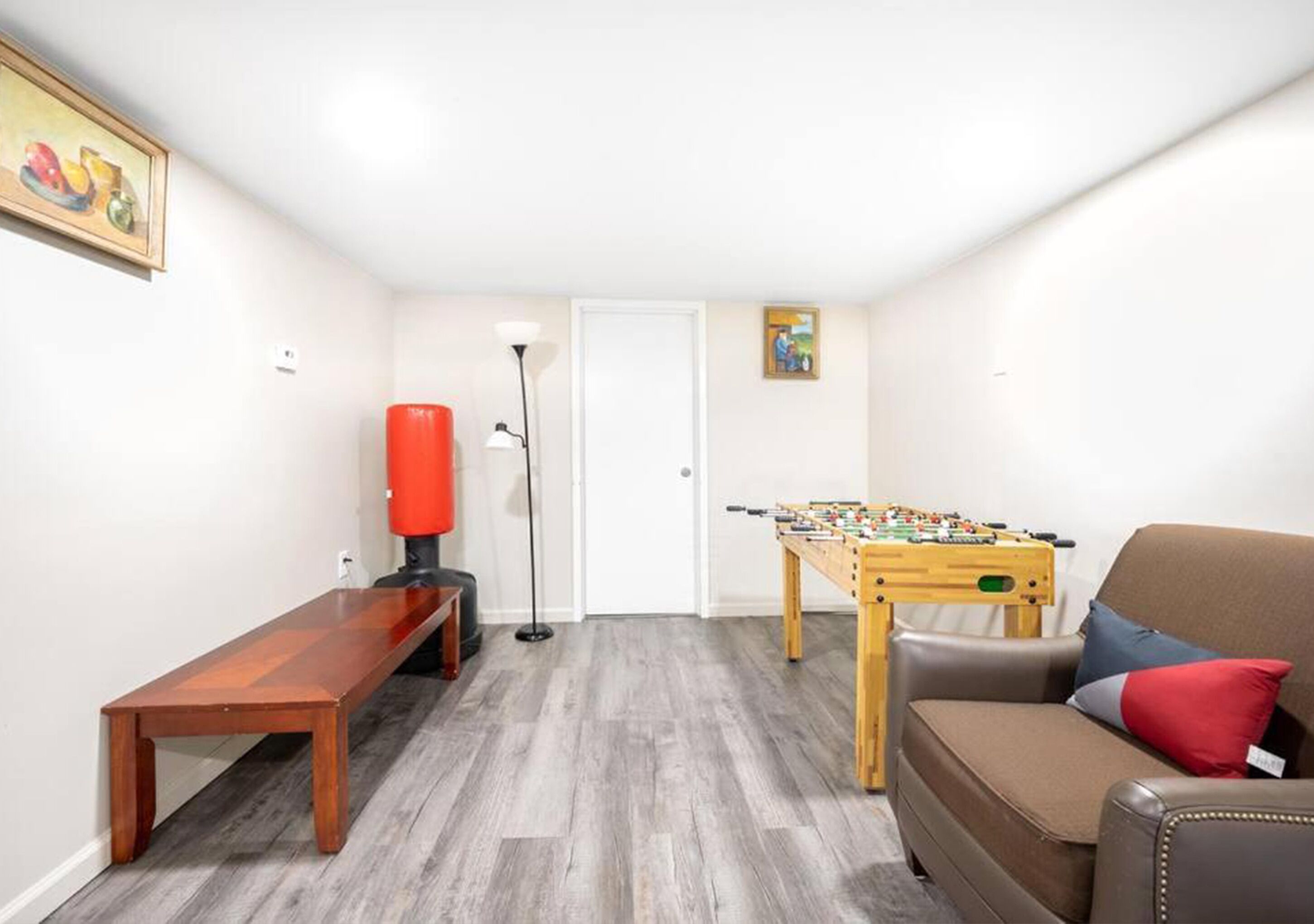 Ett rum med ett fotbollsspel, en bänk, en soffa med en röd kudde och en golvlampa.