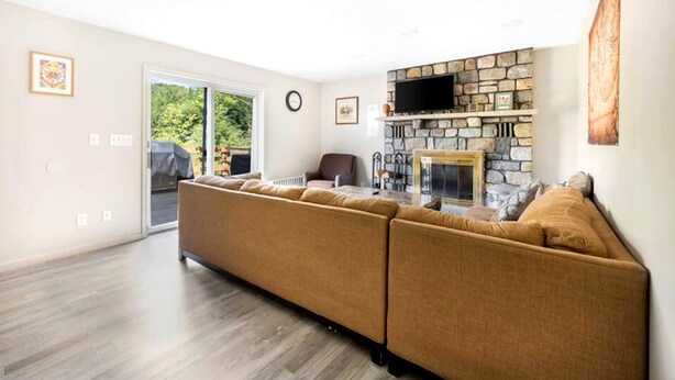 A modern living room with a stone fireplace, a large sectional sofa, and a television mounted above it. - Garden View Home (Tobyhanna)