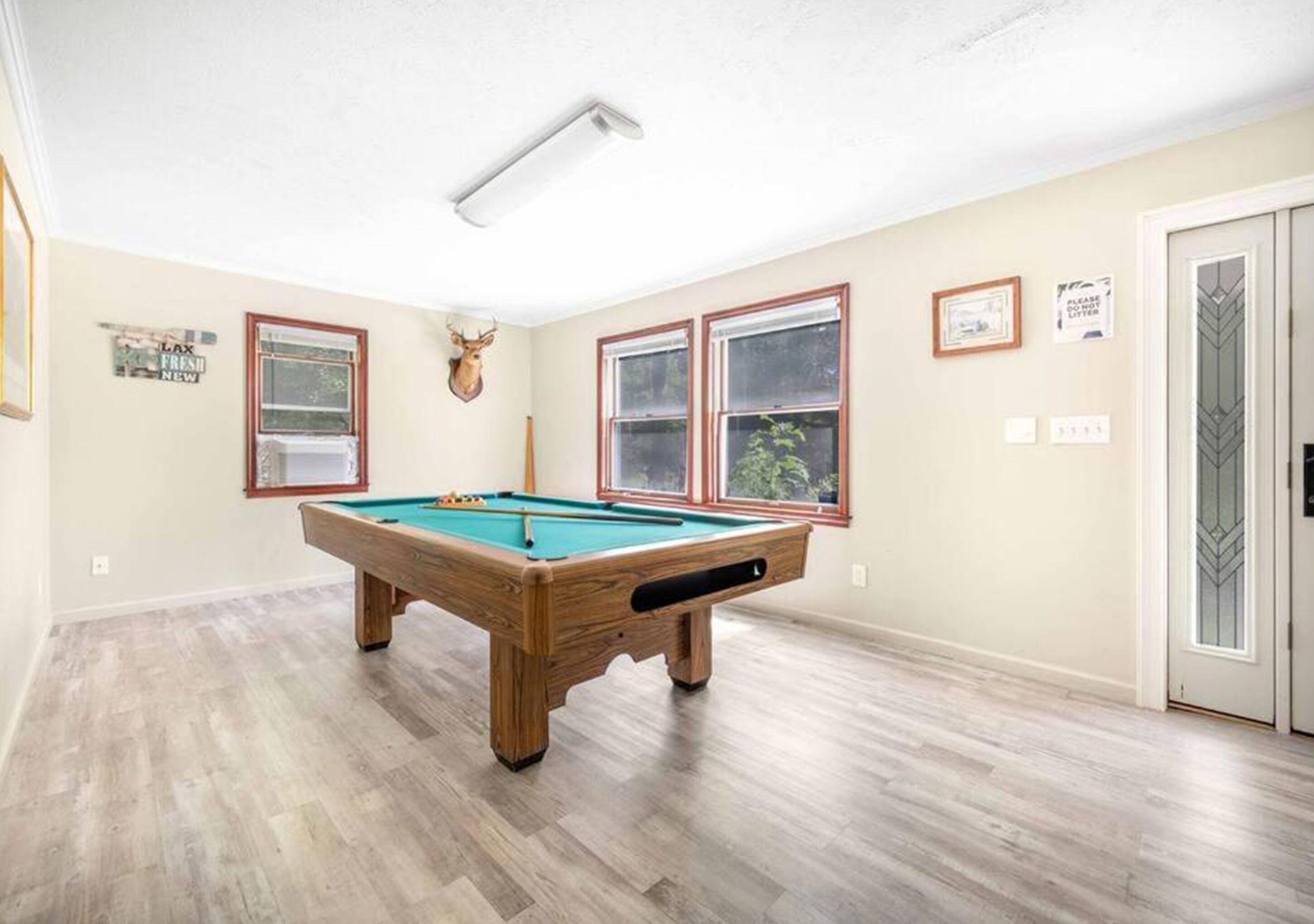 A pool table in a room with wooden flooring, two windows, and a door with a decorative glass panel.