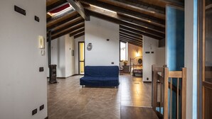 A spacious room with a blue sofa, wooden beams, and a tiled floor. - Villa Cavalieri in Vedriano with a panoramic view of the Reggio Emilia hills (Canossa)
